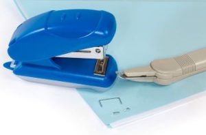A small blue stapler and a staple remover are sitting on top of some papers that are stapled together in the corner.